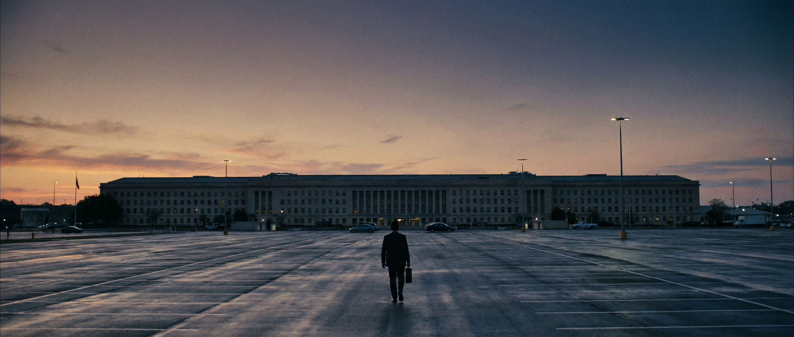 A silhouetted figure walking away from the Pentagon at dusk, briefcase in hand